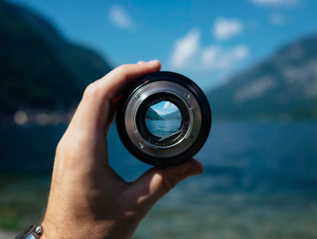 A hand holding a looking glass by a lake